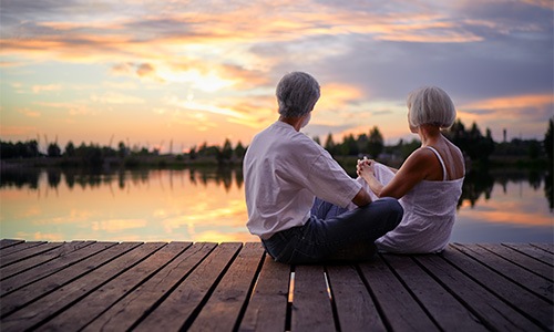 two people sitting on a dock looking at the sunset